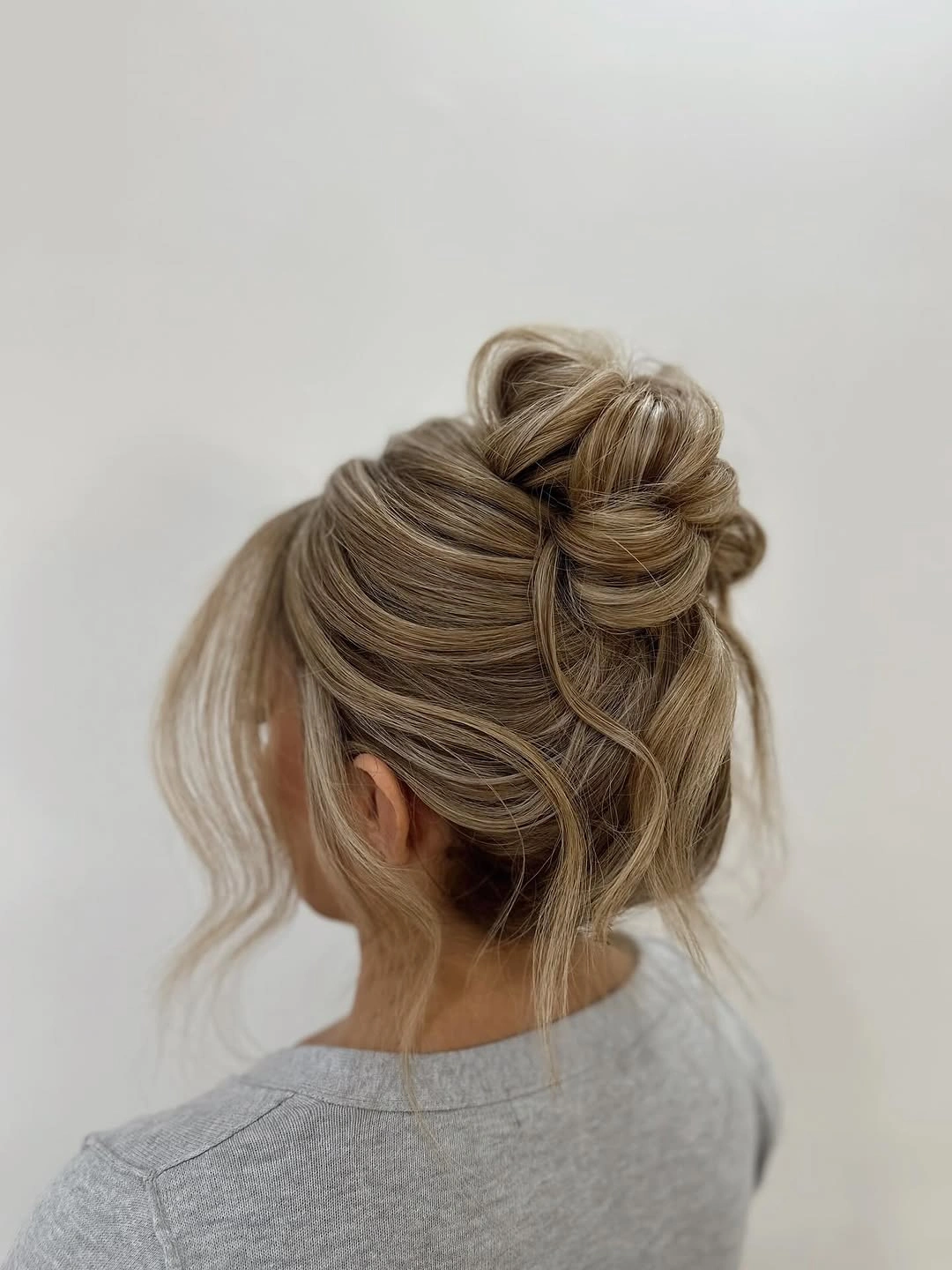 fall hairstyles for wedding guests 2026 Relaxed High Bun With Wispy Pieces
