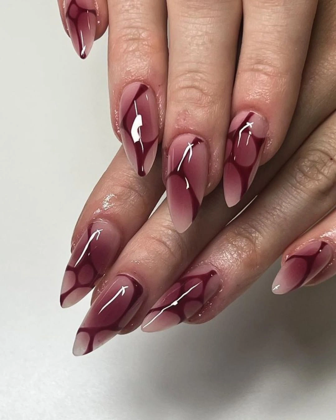 stylish maroon fall nails 2026 Glossy Burgundy Almond Nails With Abstract Details