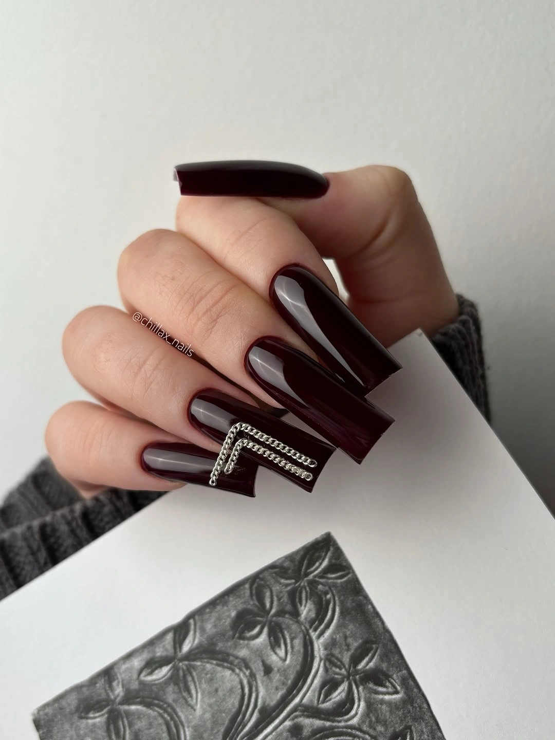 trendy fall nails for fair skin tone - glossy burgundy nails with silver chain accents